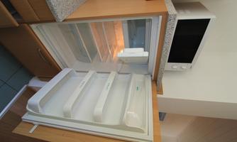 An open refrigerator with empty shelves. In the background, a microwave is visible.