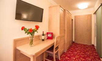 A cozy room with wooden paneling and a television on the wall. On the table, there is a vase with roses and a bottle of wine.
