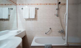 A modern bathroom with a bathtub and a shower. Fresh towels hang on the wall, and the room is bright and clean.