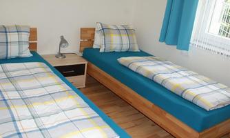 A bright bedroom with two single beds and blue bedding. Next to the beds is a nightstand with a lamp.