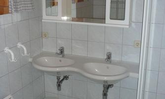 A modern bathroom with a double sink and a large mirror. There is a shower and tiled walls.