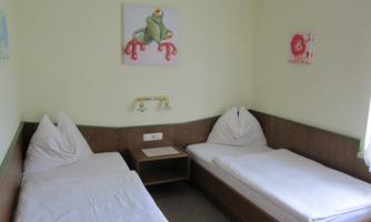 A simple room with two single beds and colorful wall paintings. The walls are light green, and the room feels friendly and inviting.
