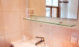 A modern bathroom with a white sink and a large mirror. Yellow towels are neatly placed on the shelf.