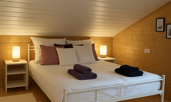 A cozy bedroom with a white bed and gentle lighting. The walls are made of wood, and there are stylish pillows on the bed.
