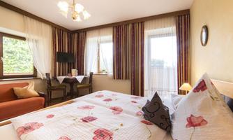 A cozy bedroom with a double bed, decorated with floral patterns. The room has large windows and an inviting seating area.