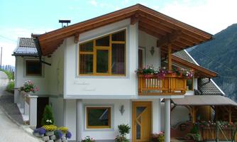 A modern house in the mountains with a wooden roof and a balcony. Colorful flowers decorate the exterior and give the house a welcoming atmosphere.
