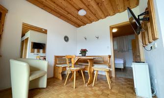 A cozy room with wooden floor and ceiling. There is a table with chairs, a television, and a seating area.
