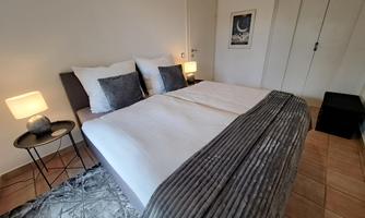 A cozy bedroom with a large double bed and modern pillows. Next to the bed are nightstands with lamps and there is a carpet on the floor.