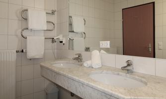 A simple bathroom with two sinks and a large mirror. Fresh towels are hanging on the wall, and the walls are brightly tiled.