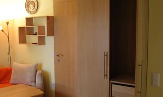A small living room with a wooden cabinet and an orange sofa. The walls are painted in a light shade.