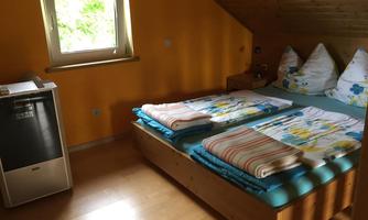 A cozy room with a double bed and colorful bedding. The walls are painted in warm yellow, and there is a window overlooking the outdoors.
