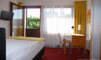 A bright and cozy hotel room with a large window and a balcony. The room is modernly furnished and features a dining area with a table and chairs.