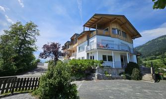 A modern building with a wooden-clad facade and a balcony.  
Surrounded by green trees and a beautiful landscape.