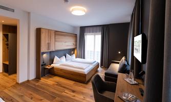 A modern bedroom with two beds and wood-paneled furniture. The room has large windows and a desk with a television.