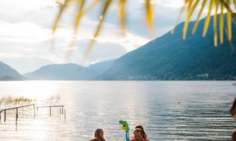 A group of people at the beach with inflatable swim toys. In the background, there is a calm lake and mountains visible.