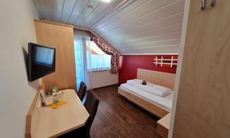 A modern room with a single bed and a desk. The room is bright and friendly with a television on the wall.