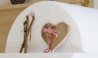 A decorative wooden heart with a red and white ribbon stands on a white surface. Next to it lie two old ski poles, conveying a cozy atmosphere.