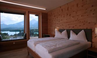 A modern room with wooden paneling and two beds. Large windows offer a view of the mountains and the lake.