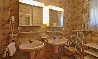 A small bathroom with two sinks and two mirrors. The walls are tiled and there are some shelves.