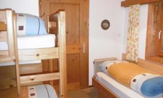 A cozy bedroom with a loft bed and a single bed. The walls are made of wood and the room is well-lit.