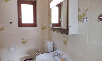A modern bathroom with a white sink, a mirror, and a small window opening. The walls are decorated with light tiles and a subtle floral pattern.