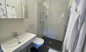 A modern bathroom with a shower and a sink. Towels hang on the walls, and the space is bright and clean.