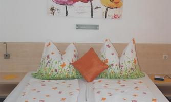 A cozy bedroom with a large bed and colorful bed linens. An artwork with red and yellow flowers hangs on the wall.