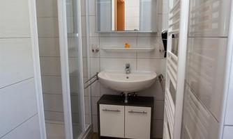 A modern bathroom with a shower, sink, and a mirror. The floor is covered with a carpet and the walls are brightly tiled.