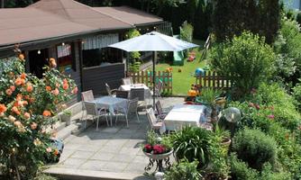 A beautifully designed garden with a cozy seating area and a sunshade. Surrounded by many colorful flowers and green plants.