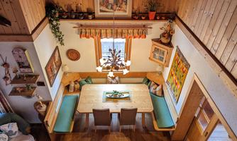 A cozy dining area with wooden paneling and a large table. Surrounded by colorful pictures and plants, the decor creates an inviting atmosphere.