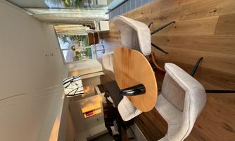 A modern dining room with a round wooden table and comfortable chairs. Large windows provide plenty of daylight and a view of the outdoors.