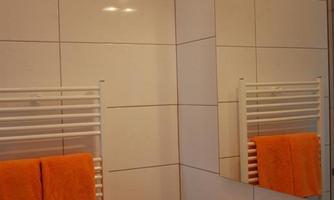 A modern bathroom with bright tiles and a smooth wash surface. Orange towels provide a colorful accent.