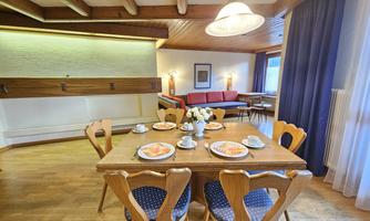 A cozy dining area with a wooden table and chairs. Plates, cups, and a flower vase are arranged on the table.