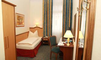 A cozy hotel room with a single bed and a desk. Large windows with colorful curtains let in a lot of light.
