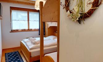 A cozy bedroom with two beds and wooden details. There is a window view of the garden and a decorative wall crown made of flowers.