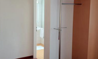 A bright room with an open wardrobe and a door leading to a bathroom. The floor is carpeted, and the walls are in neutral colors.