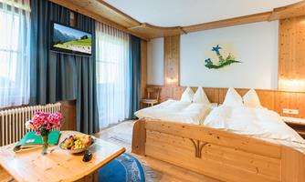 A cozy bedroom with wood paneling and two beds. On the table, there is a fruit bowl and fresh flowers.