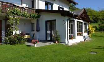 A beautiful house with a well-maintained garden. The terrace is equipped with plants and a sunshade.