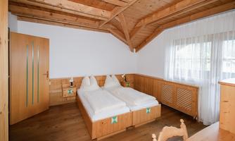 A cozy bedroom with two wooden single beds. The room has a wooden ceiling and large windows that let in plenty of light.