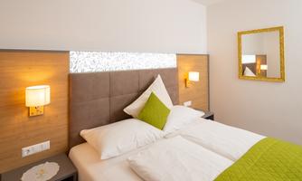 A cozy bedroom with a comfortable bed and modern lamps. The walls are in warm tones, and a mirror adds extra charm to the room.