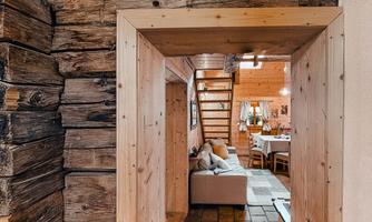 A cozy room with wood paneling and an open view of the kitchen. A staircase leads to the upper floor.