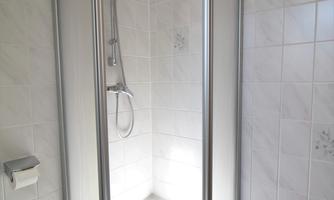 A modern glass shower cabin with a silver frame. The walls are tiled, and the furnishings are simple and elegant.