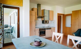 A modern kitchen with wooden furniture and an open connection to the living area. The dining area is bright and inviting, with access to a terrace.