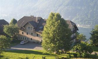 A tranquil house surrounded by lush greenery and trees, with a scenic view of the landscape in the background. A car is parked nearby, adding to the serene setting.