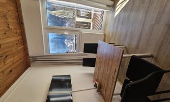 A bright kitchen with a wooden table and black chairs. Large windows provide a view outside and plenty of daylight.