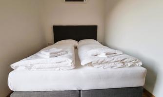 A modern bedroom with a double bed. The bedding is neatly folded and the walls are painted light.