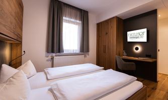 A modern bedroom with two single beds and a warm wood design. There is a television on the wall and a desk.