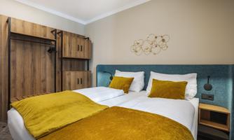 A stylish room with two single beds and a modern design. The yellow cushions and wooden details create a cozy atmosphere.