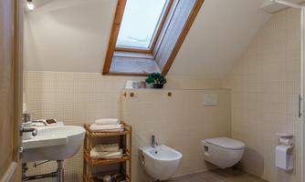 A modern bathroom with a roof window and simple tiles. There is a sink, a toilet, and a small shelf with towels.