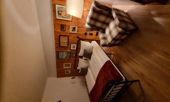 An inviting bedroom with a double bed and a cozy armchair. Decorative pictures hang on the wall, and a lamp provides warm light.